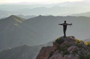 A person stands on top of a mountain with their arms outstretched.