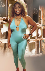 A Black woman with medium-length curly hair wearing a turquoise bodysuit smiles at the camera.