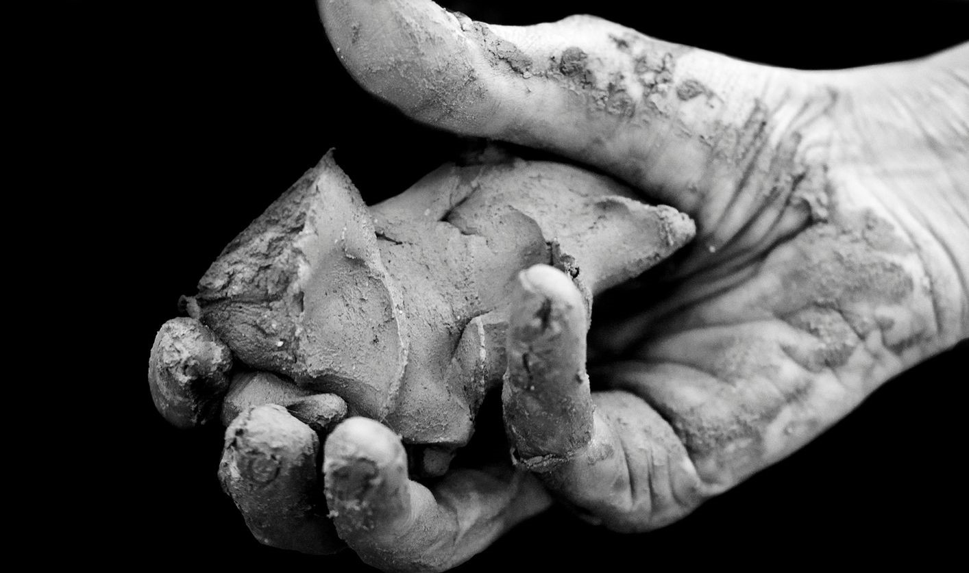 A black and white image of a hand holding a lump of clay.