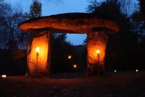 A stone megalith at dusk is light up by two torches.