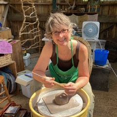 A smiling white woman works with clay on a wheel.